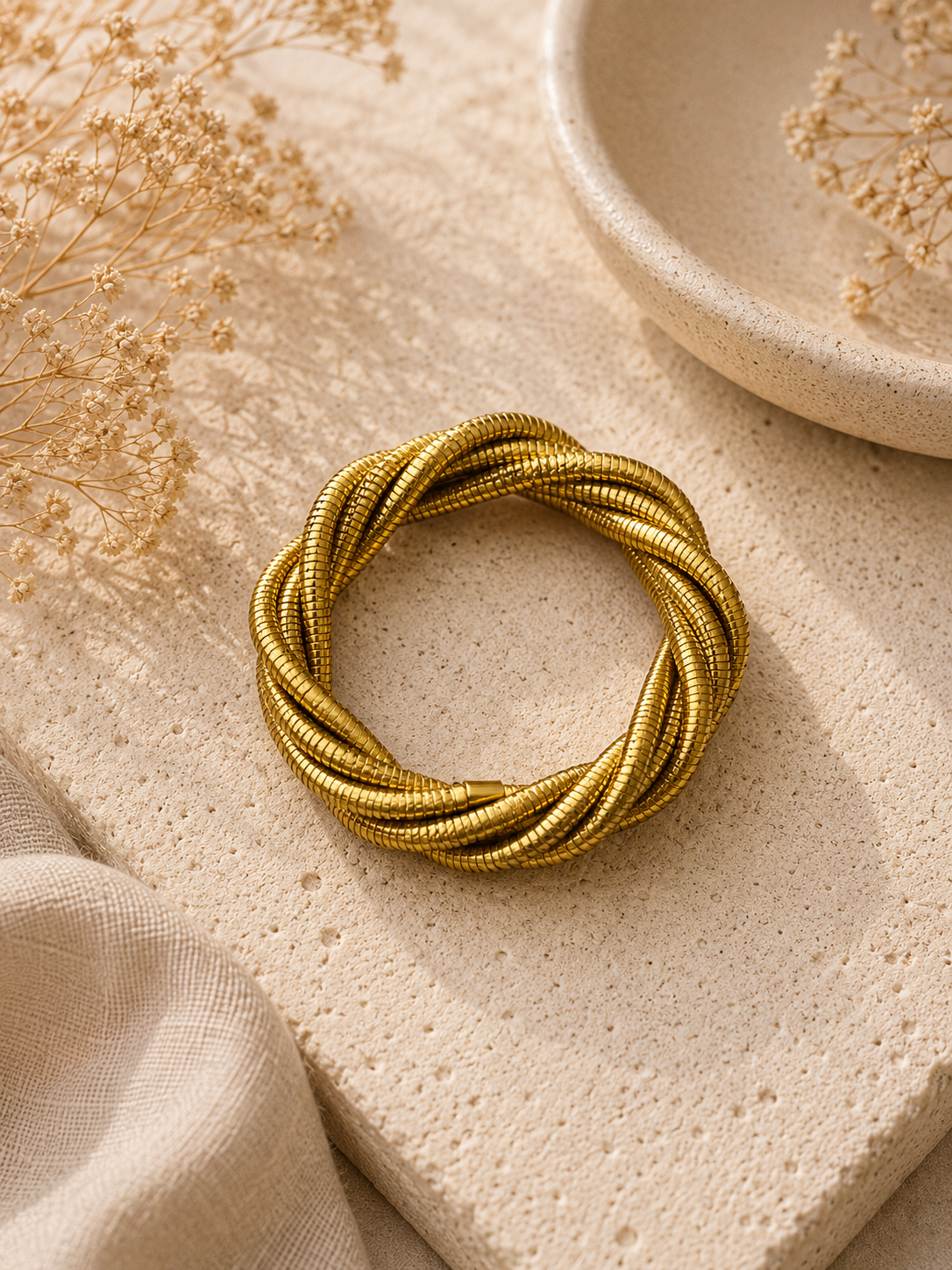 Pulsera trenzada dorada tipo snake sobre piedra
