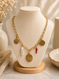 Collar dorado chunky con charms de sol, perla barroca, medallón floral ovalado, cornetto rojo y moneda grabada sobre busto de exhibición