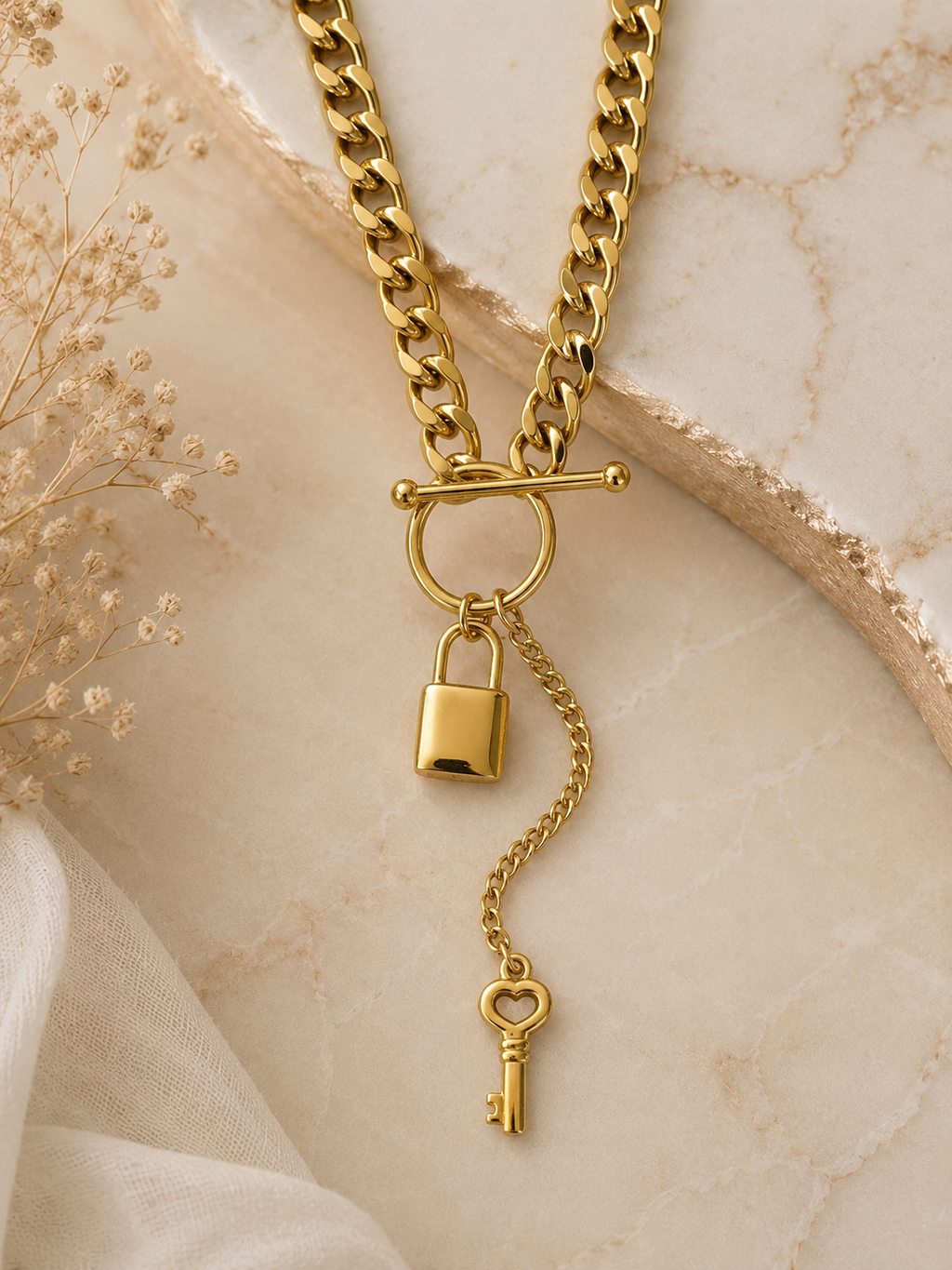 Collar cadena cubana dorada con candado y llave sobre mármol