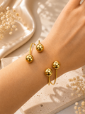 Brazalete rígido dorado abierto con esferas pulidas en la muñeca