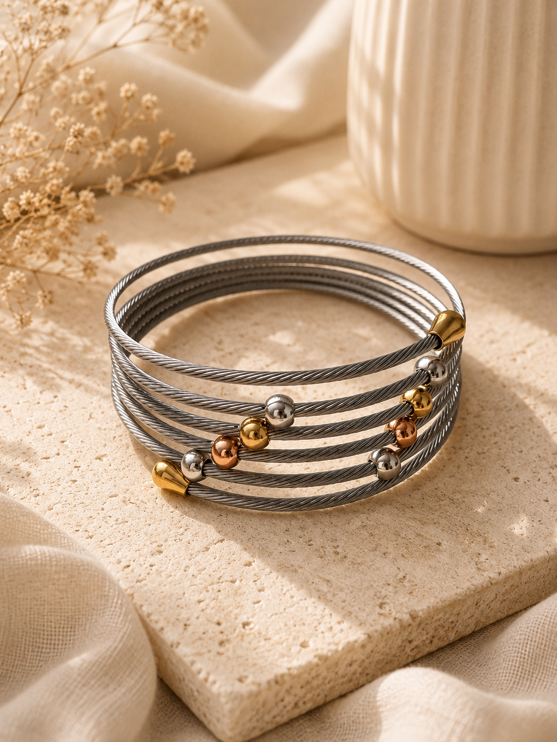 Pulsera de cable trenzado plateado con esferas tricolor sobre piedra