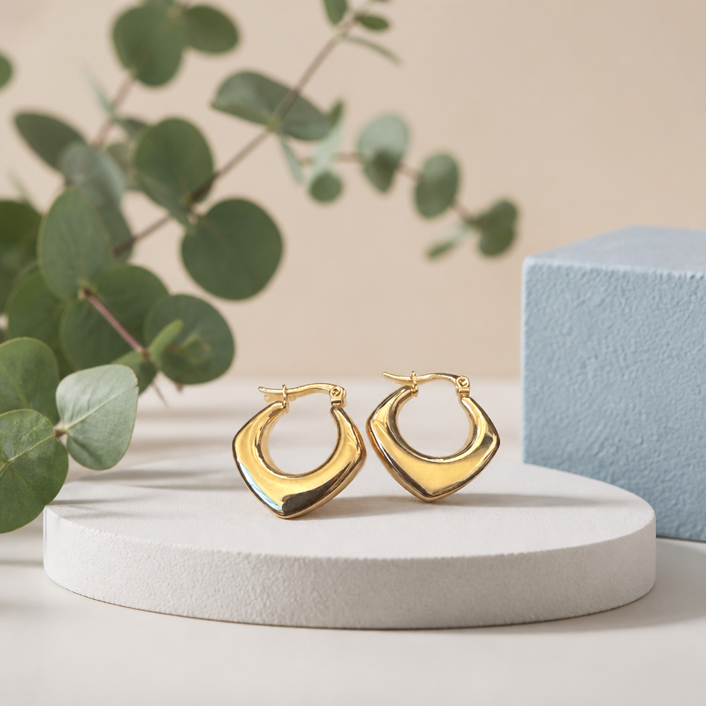 Aretes argolla cuadrada gold de acero inoxidable sobre pedestal blanco con eucalipto