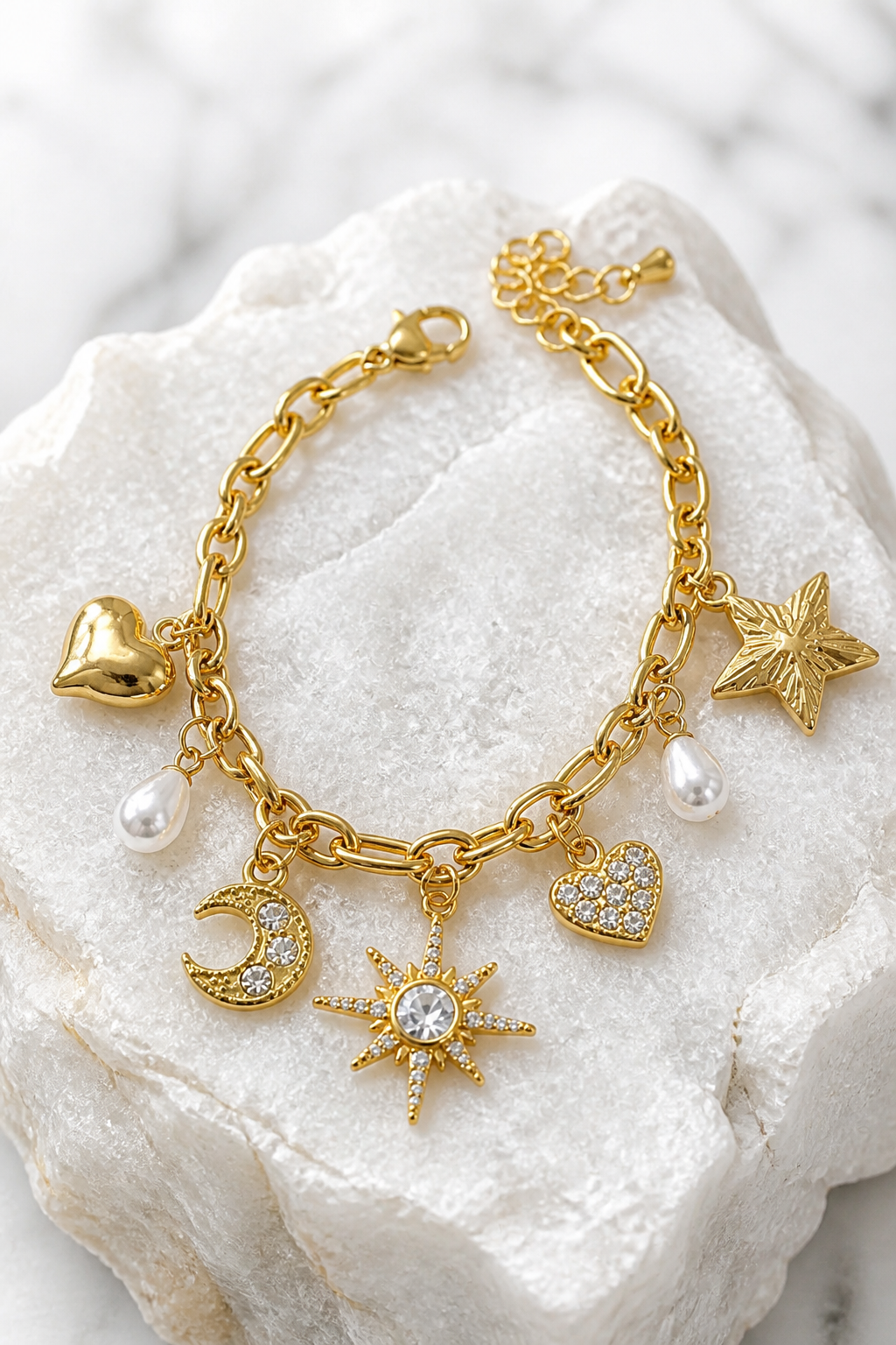 Pulsera dorada con charms celestiales de luna con cristales, estrellas, corazones y perlas sobre piedra blanca